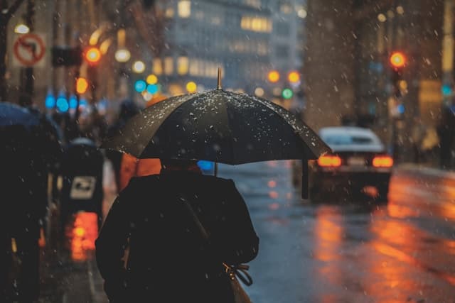 Uma pessoa usando um casaco preto segura um guarda-chuva enquanto uma chuva forte cai ao seu redor,  transmitindo uma sensação de desorientação e solidão em meio à tempestade.